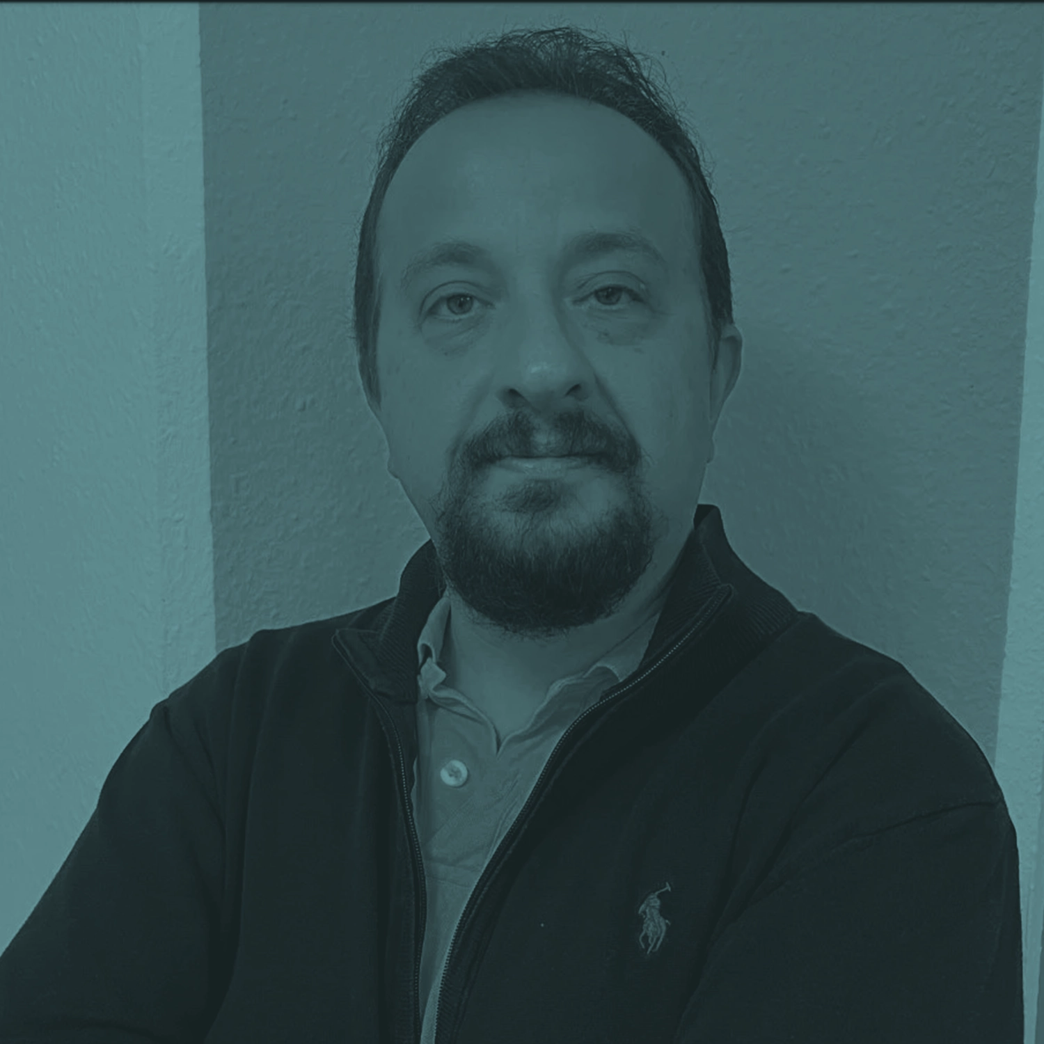 Porträt von Ibrahim Dilek mit verschränkten Armen vor neutralem Hintergrund.